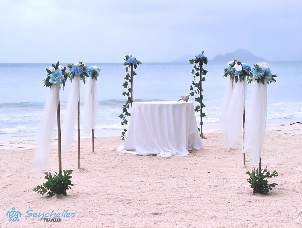 Kék művirágokkal díszített bevonuló folyosó és esküvői asztal Anse Louis tengerparton.