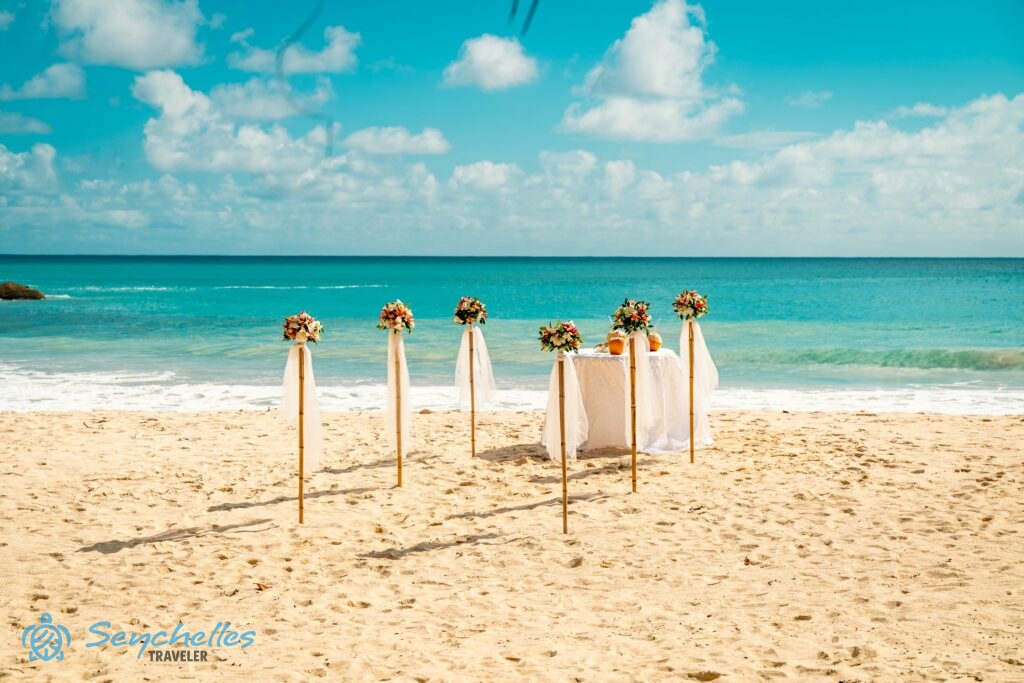 Bevonuló folyosó színes frangipáni virágokkal díszített bambusz oszlopokkal és esküvői asztal Anse Louis tengerparton.