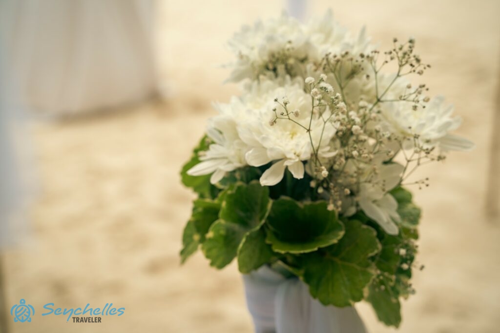 A bevonuló folyosó bambusz oszlopait díszítő fehér krizantémból és rezgőből álló virágcsokor Baie Lazare tengerparton.