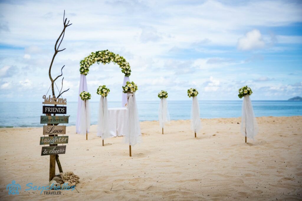 Fehér virágcsokrokkal díszített bevonuló folyosó és virágokkal dúsan díszített, íves boldogságkapu Anse Louis tengerparton.