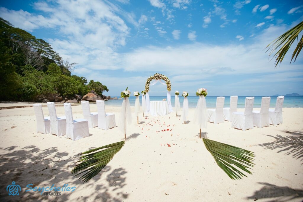 Virágokkal díszített bambusz oszlopokból álló bevonuló folyosó boldogságkapuval, mellette fehér székek, Anse Louis parton.