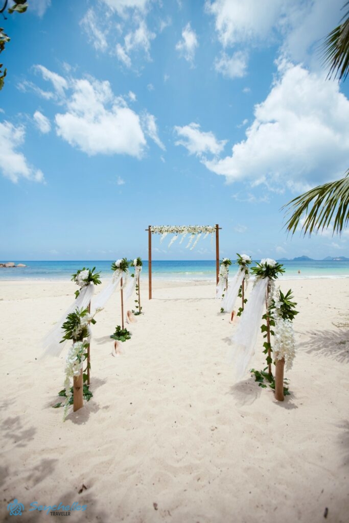 8 oszlopból álló bevonuló folyosó fehér dekorációval, közöttük tengeri csigaházak a homokban és szögletes boldogságkapu.