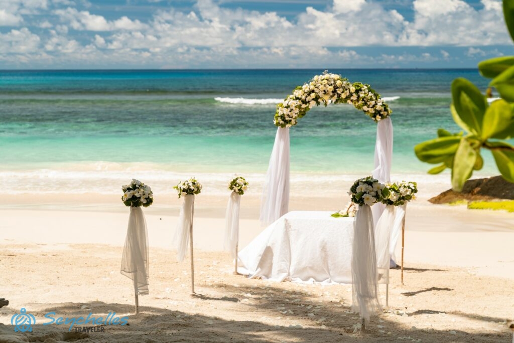 Gömb alakú csokorral díszített oszlopokból álló bevonuló folyosó, íves boldogságkapu fehér virágokkal és esküvői asztal.