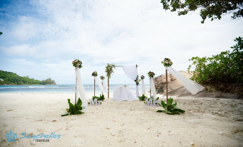 Gömbcsokorral és a homokban zöld levelekkel díszített, 6 oszlopos bevonuló folyosó, szögletes boldogságkapu, esküvői asztal.