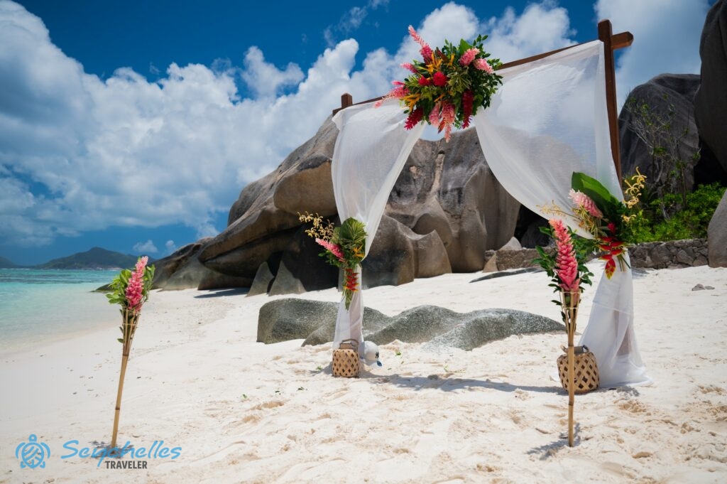 Trópusi virágokkal és fehér muszlinnal díszített szögletes boldogságkapu és bevonuló folyosó La Digue-en.