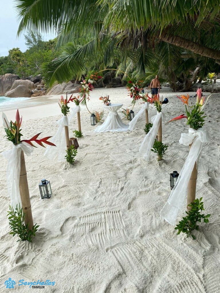 Bevonuló folyosó bambusz oszlopokkal és mécsesekkel, gyűrű alakú boldogságkapu és esküvői asztal Praslin-en.