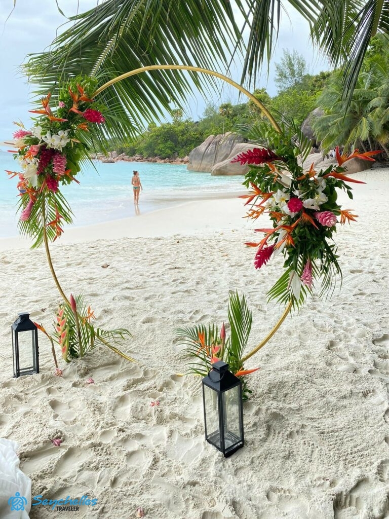 Arany színű, gyűrű alakú boldogságkapu a két oldalán nagy, trópusi virágokból készült díszítéssel Praslin-en.