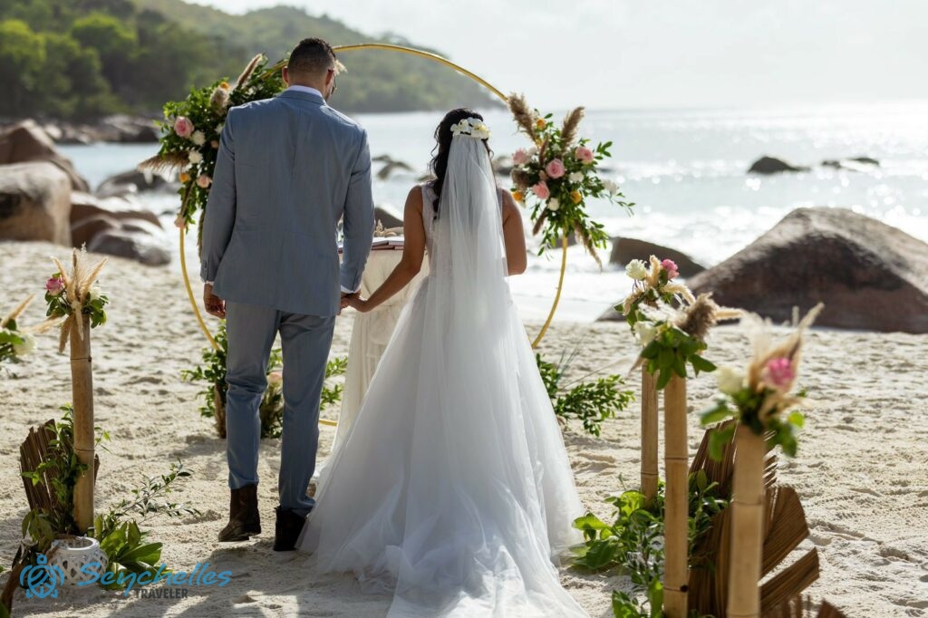 Az ifjú pár áll a gyűrű alakú boldogságkapu előtt, melyen virágdíszek vannak, mögöttük dekoratív bevonuló folyosó.