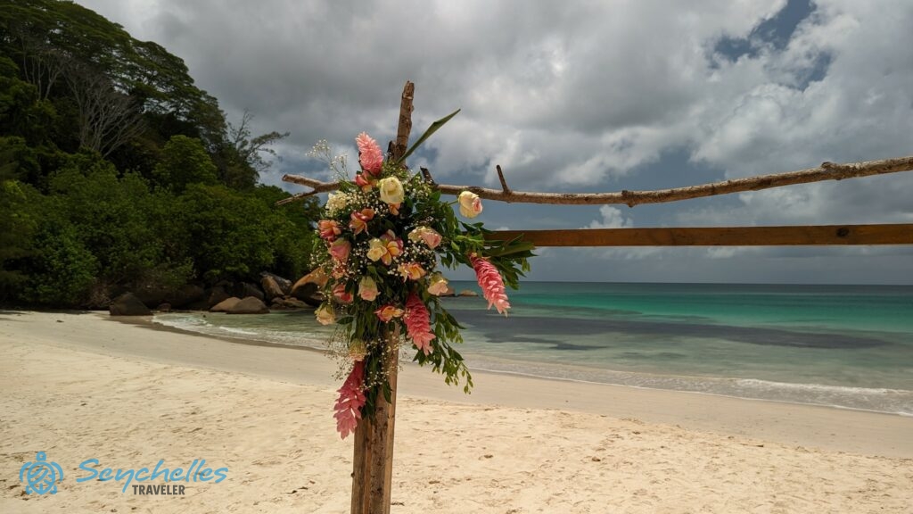 Rózsaszín és törtfehér virágokból készült dísz a szögletes boldogságkapun Anse Louis tengerparton, Mahén.