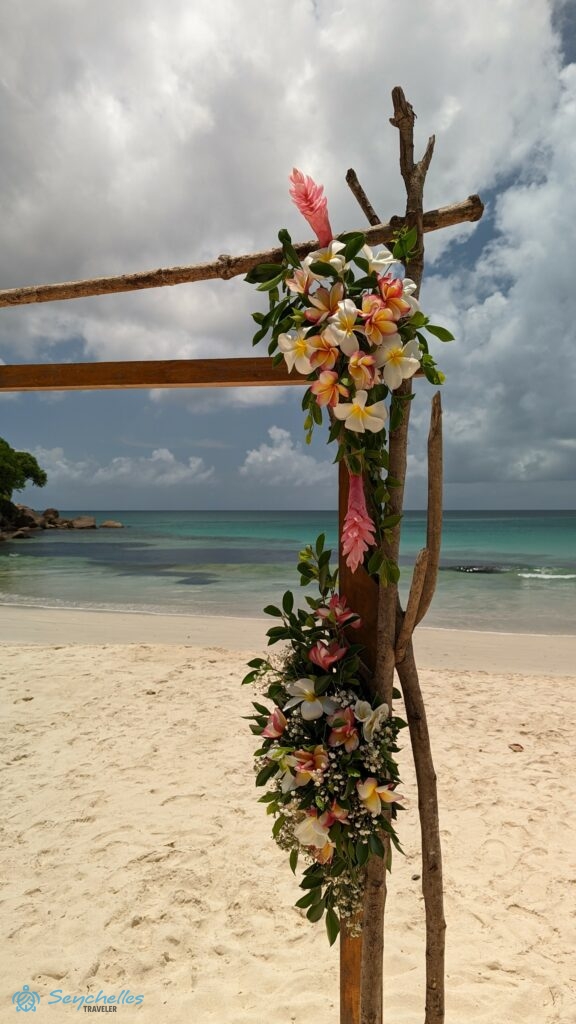 Frangipáni és gyömbér virágokból, valamint zöld levelekből álló boldogságkapu dekoráció Anse Louis tengerparton, Mahén.