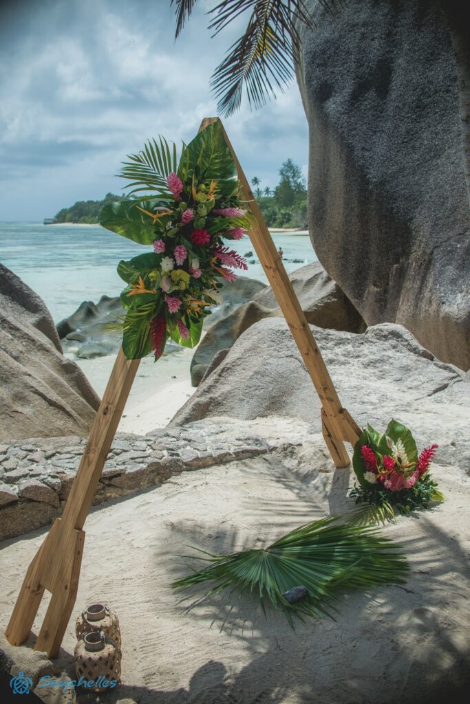 Háromszög alakú boldogságkapu színes gyömbér és papagájvirágokkal, monstera levelekkel La Digue-en.