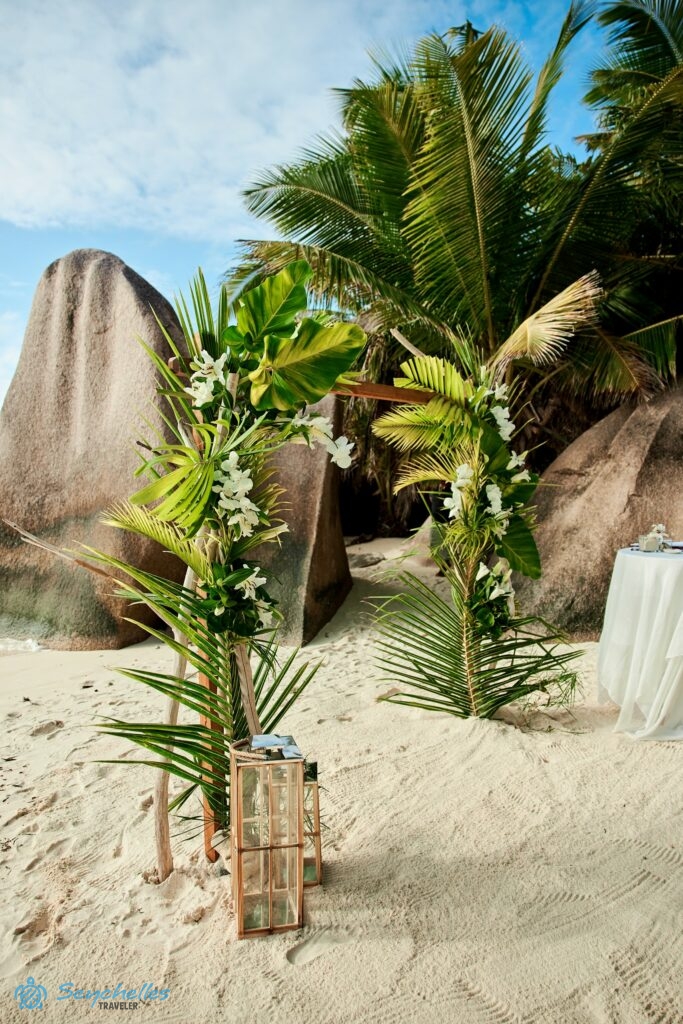 Trópusi levelekkel és fehér orchideákkal díszített szögletes boldogságkapu La Digue-en, a gránitsziklák tövében.