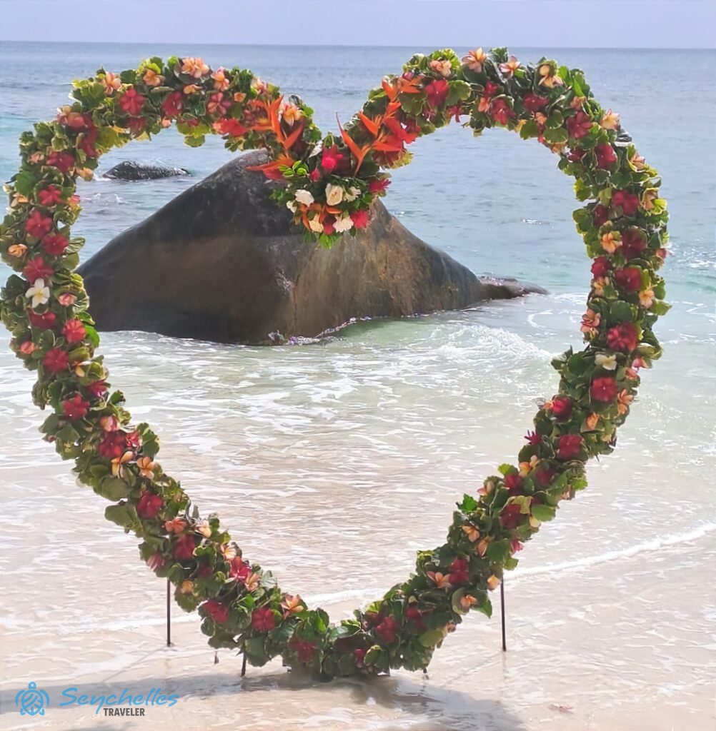 Szív alakú, színes trópusi virágokkal és levelekkel díszített boldogságkapu Mahén, a háttérben gránitsziklával.