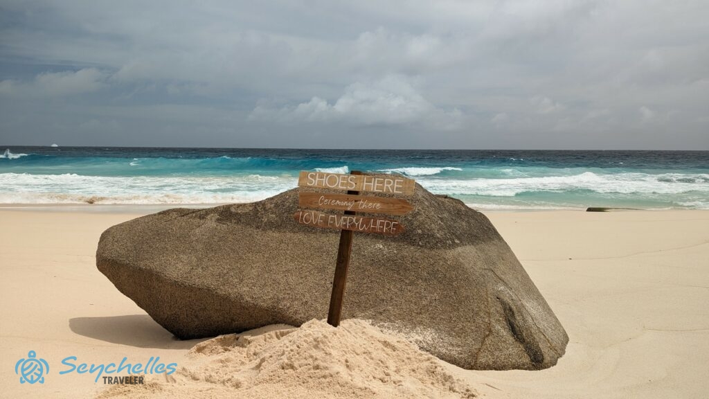 Gránitszikla és üdvözlő tábla a homokban Anse Bazarca esküvői helyszínen.