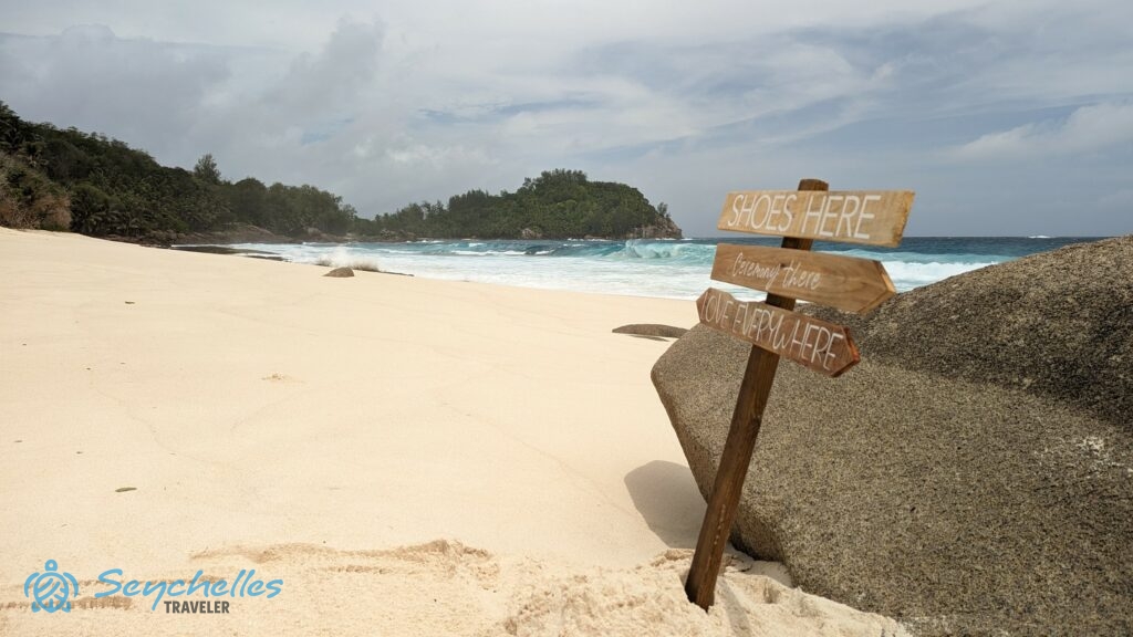 Anse Bazarca esküvői helyszín üdvözlő táblával, a háttérben az óceánnal.