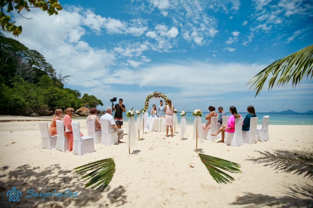 Réka egy párt esket Mahén, Anse Louis esküvői helyszínen, a bevonuló folyosó két oldalán vendégek ülnek fehér székeken.