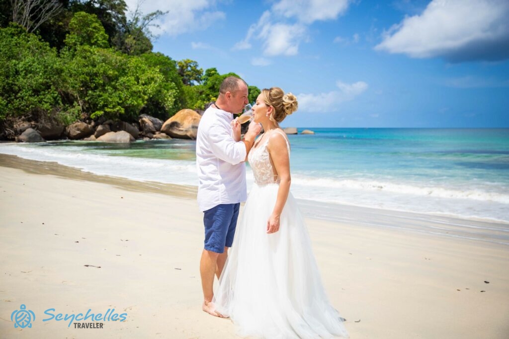 A friss házasok pezsgőt isznak Mahén, Anse Louis tengerparton a türkizkék óceán közelében.