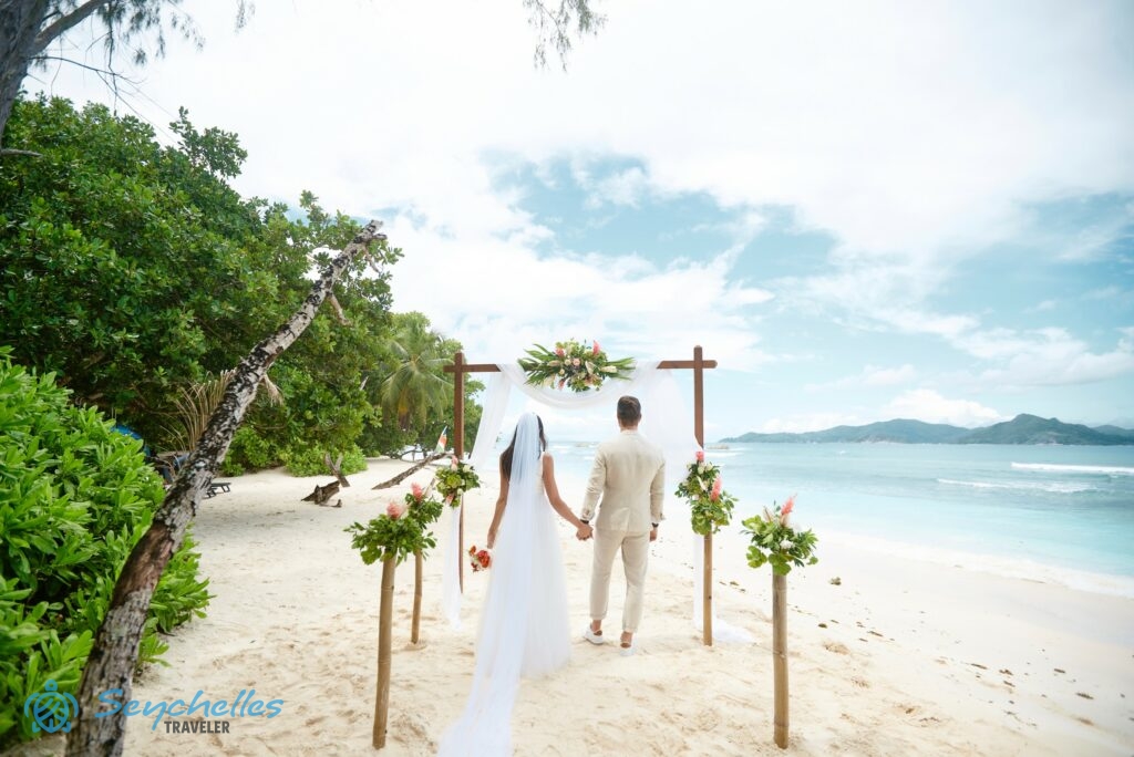 Az ifjú pár a virágokkal díszített bambusz oszlopok között halad a fehér muszlinnal és gyömbér virággal dekorált kapu felé.