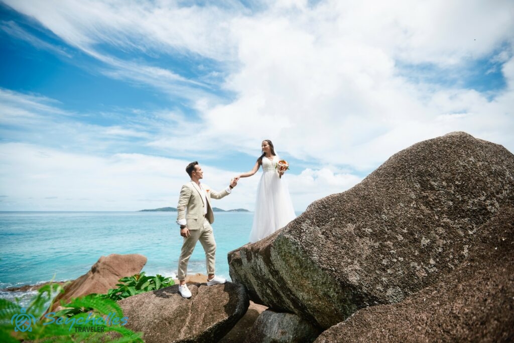 A friss házasok Anse Severe gránitszikláin állnak, mögöttük az óceán és a távolban a Nővér-szigetek látszódnak.