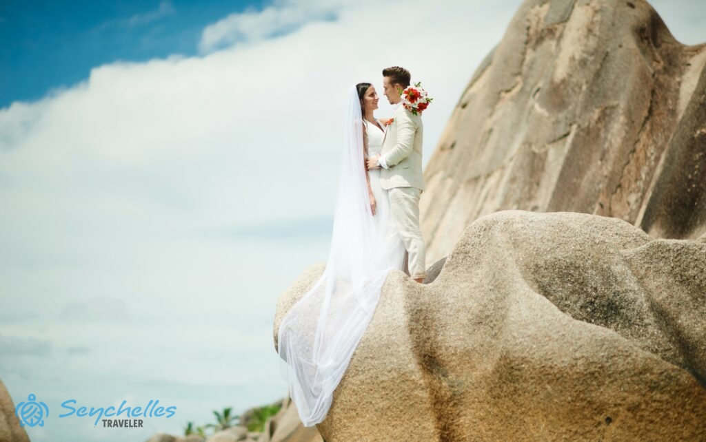 Házaspár áll egy nagy gránitsziklán Anse Source D'Argent parton, La Digue-en.