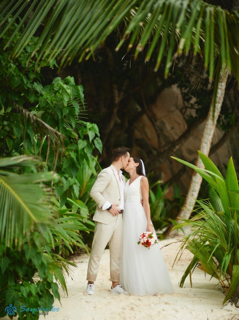 Fiatal pár a trópusi növényzettel szegélyezett ösvényen, Anse Source D'Argent parton, a háttérben gránitszikla látszódik.