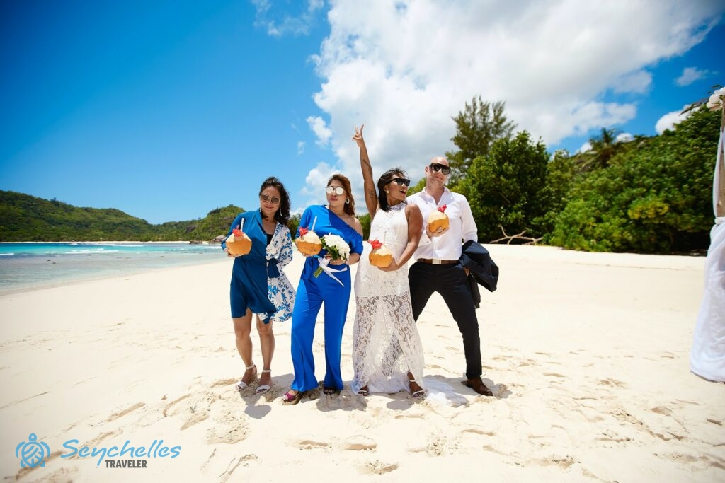 Az újdonsült házasok és tanúik friss kókuszból készült italokkal ünnepelnek Baie Lazare fehér homokos tengerpartján.