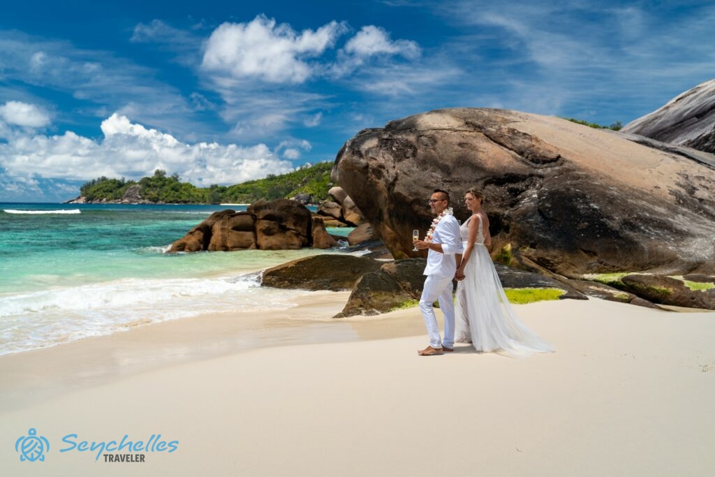A friss házasok Baie Lazare gránitsziklái mellett, a homokban állva, pezsgőspohárral a kezükben figyelik a türkizkék óceánt.