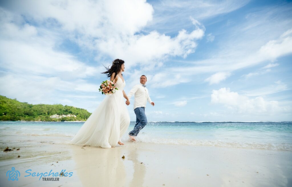 A fiatal pár a partot mosó hullámokban lépdel Baie Lazare tengerparton Mahén.