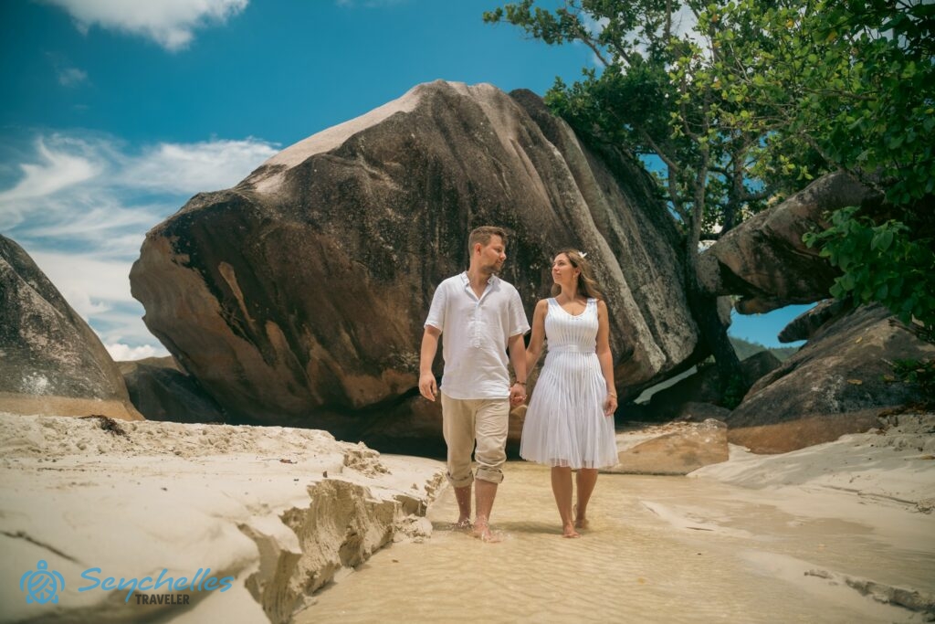 Az újdonsült házasok a gránitsziklák mögött húzódó patakban sétálnak Baie Lazare tengerparton.