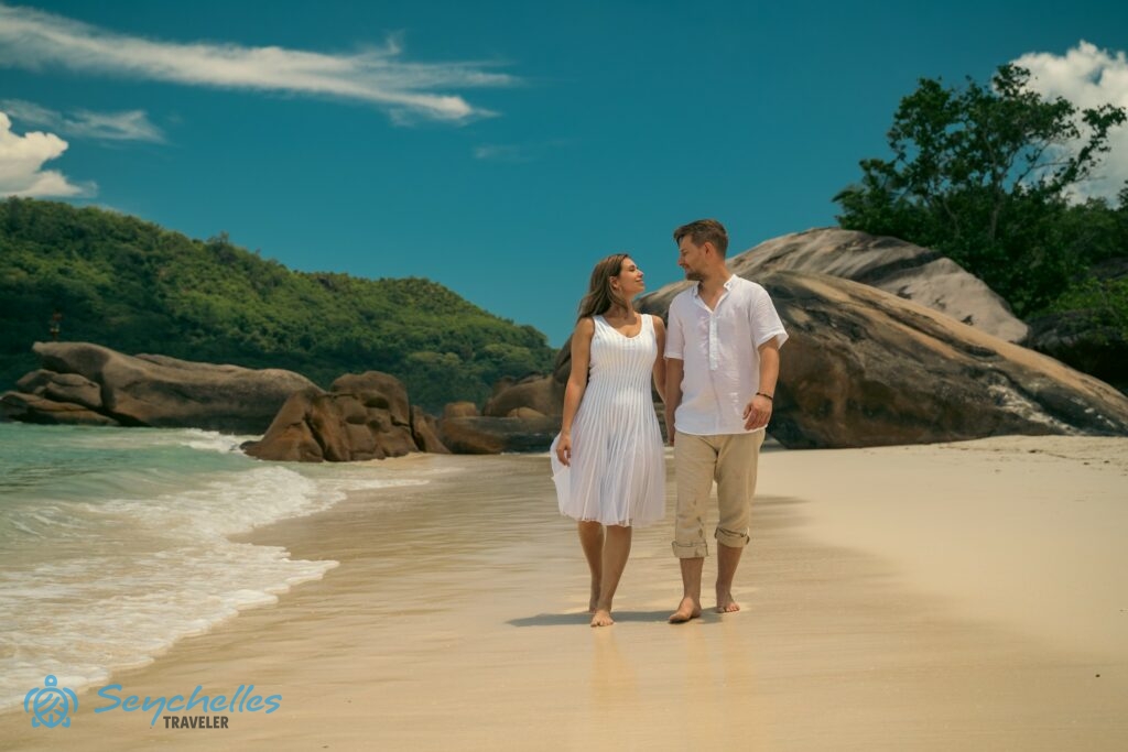 Az ifjú pár séta közben boldogan nézi egymást Baie Lazare tengerparton, Mahén.