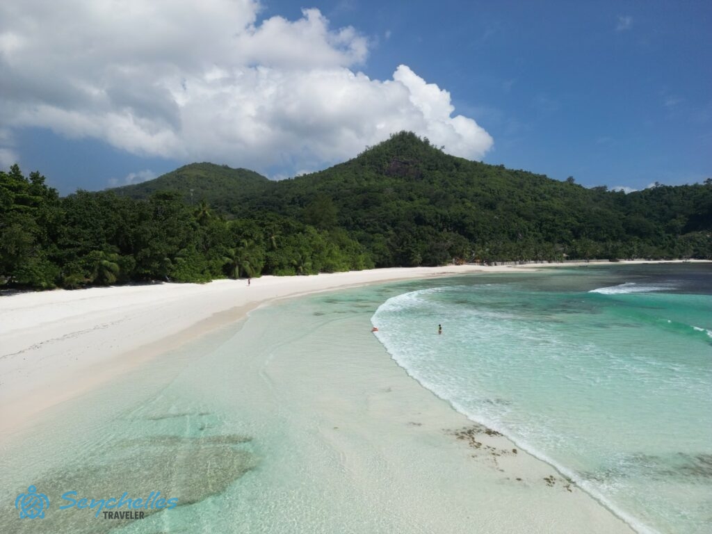 Drónfelvétel Baie Lazare fehér homokos partjáról, a sekély, kristálytiszta óceánról és a dús trópusi növényzetről.