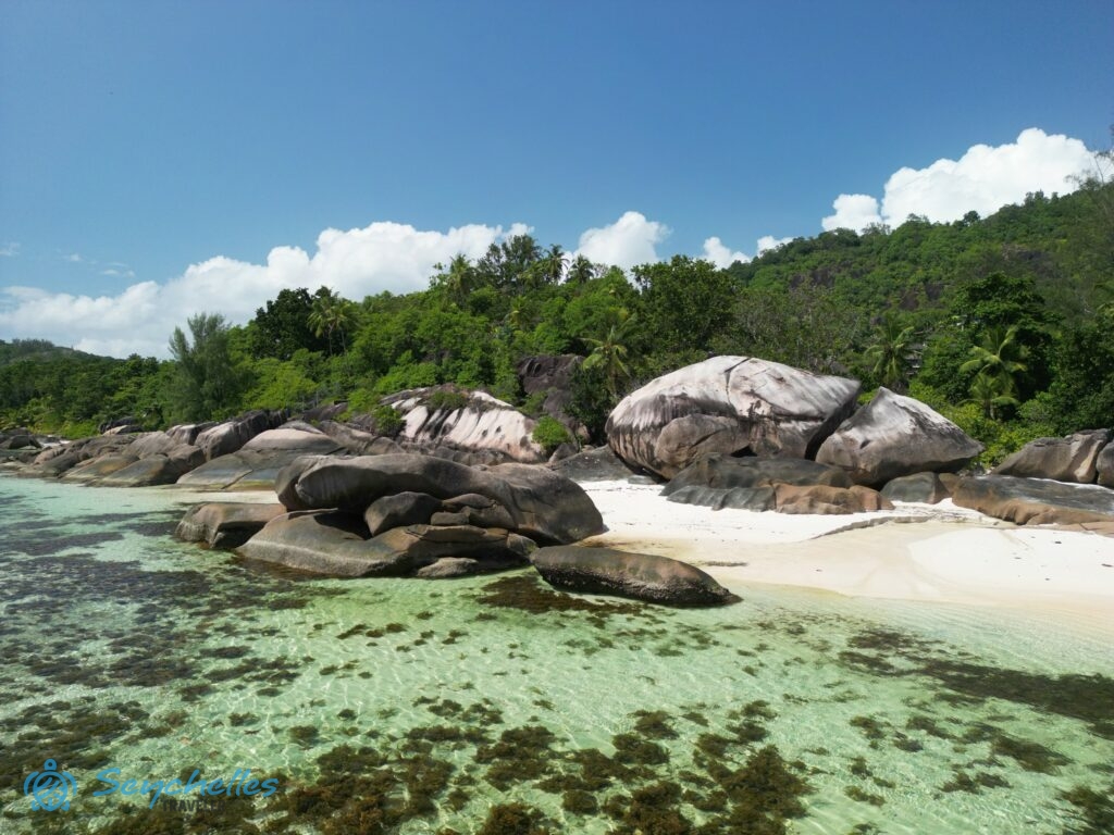A sekély vízben és a fehér homokban álló gránitsziklák a víz felől, Baie Lazare tengerparton, Mahén.
