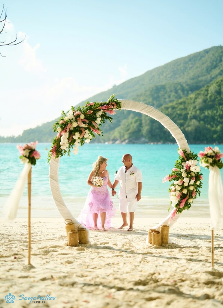 Esküvői helyszín Port Launay öbölben, Mahén. Házaspár a virágokkal díszített gyűrű formájú boldogságkapuban.