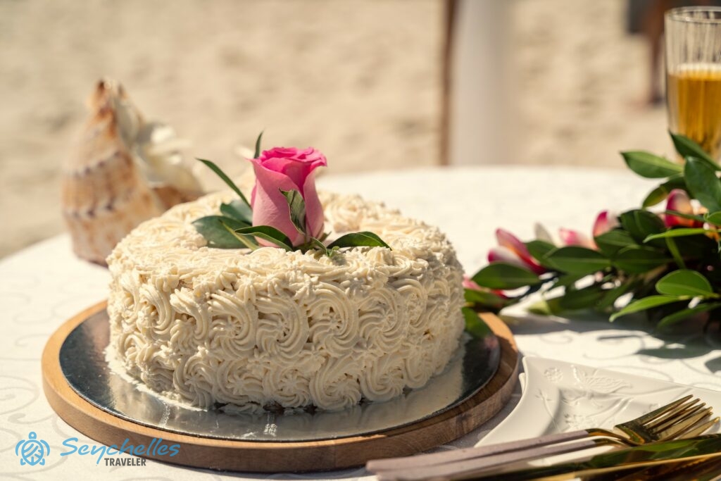 Fehér vajkrémmel díszített esküvői torta, közepén rózsaszínű rózsával Mahén.