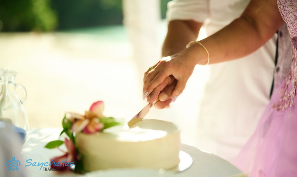 A friss házasok a fehér vajkrémmel bevont, rózsaszínű trópusi virágokkal díszített esküvői tortát szelik Mahén.