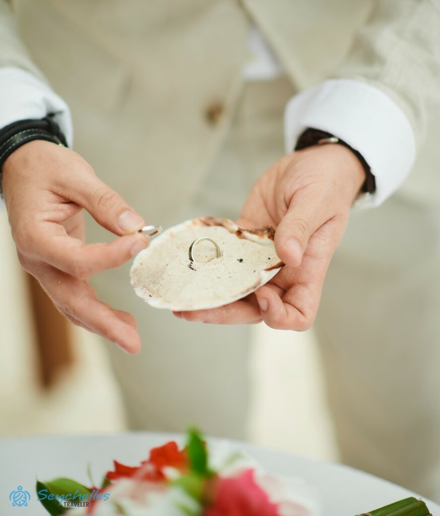 A vőlegény a homokkal teli kagyló gyűrűtartót fogja a La Digue-i tengerparti esküvőn.