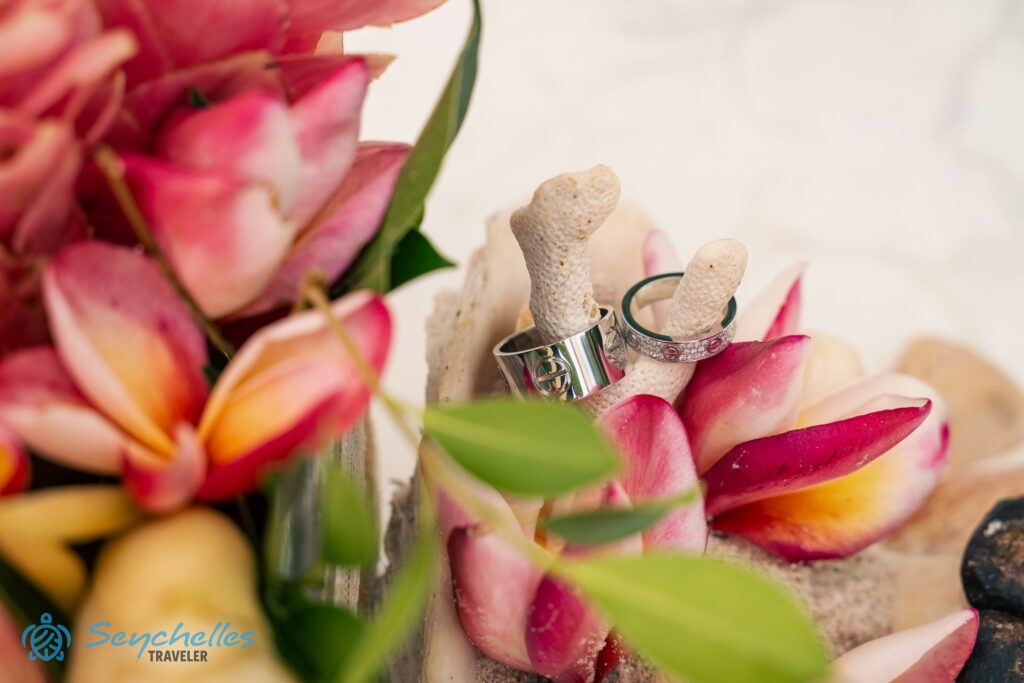 A gyűrűtartóba helyezett korall ágakra felhúzott karikagyűrűk Praslin-en, körülöttük élénk rózsaszín frangipáni virágok.