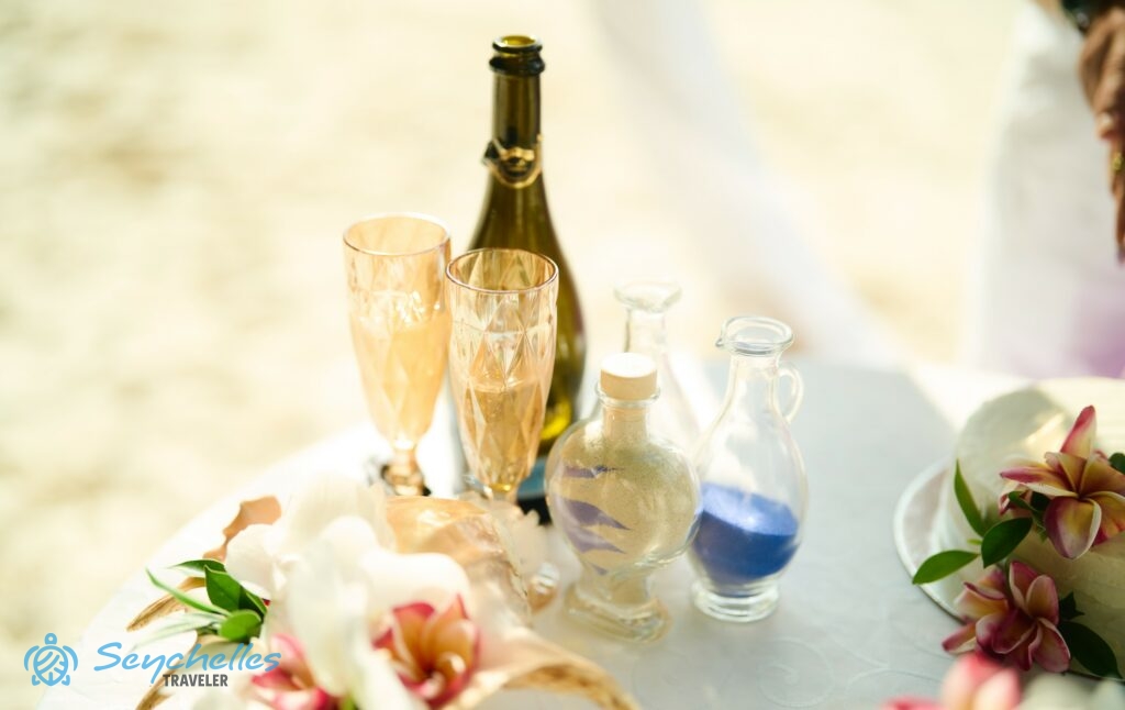 Egy üveg habzóbor két pohárral és három, homokot tartalmazó üvegcsével Mahén.