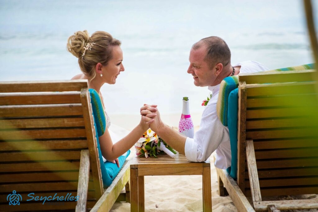 Mosolyogva nézi egymást a pár a napozóágyakon ülve, miközben kezeik összefonódnak.