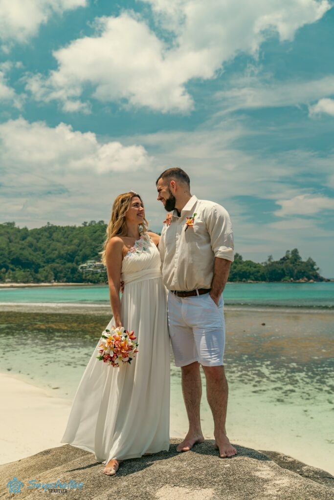 Kép a szikla tetején álló friss házasokról, mögöttük az óceánnal Baie Lazare tengerparton.