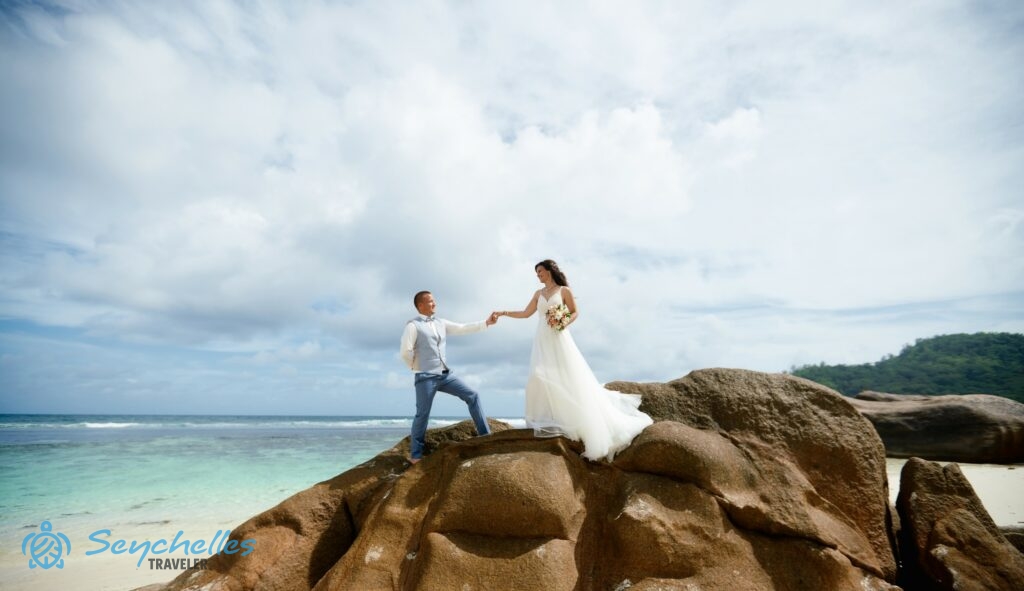 A házaspár kezüket fogva tekint egymásra egy szikla tetején Baie Lazare Tengerparton.