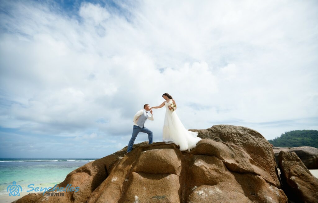 A férj megcsókolja újdonsült felesége kezét egy szikla tetején Baie Lazare tengerparton, Mahén.