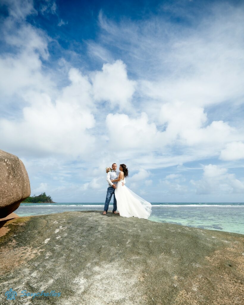 Esküvői fotó egy házaspárról Baie Lazare tengerpart egyik szikláján állva.