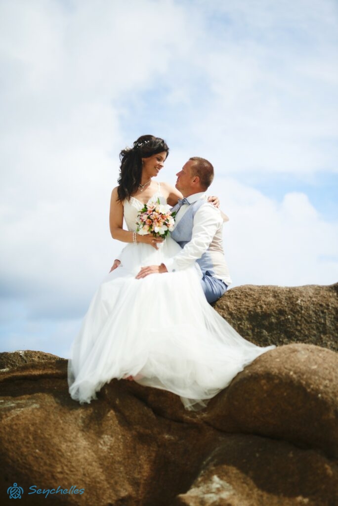 A feleség férje ölében ül egy sziklán Baie Lazare tengerparton.