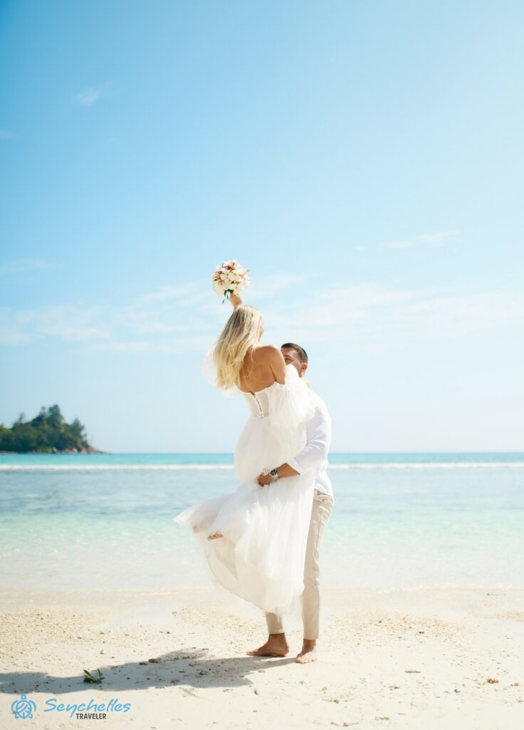 A férj Baie Lazare tengerparton a magasba emeli szőke feleségét, aki közben feltartja esküvői csokrát.