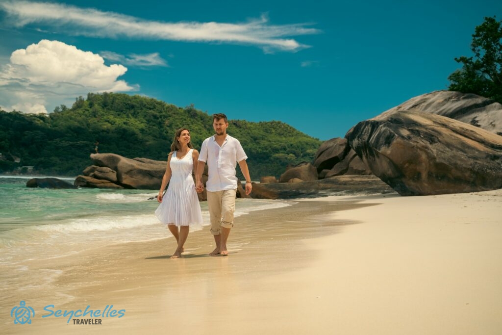 A homokban sétáló pár mögött Baie Lazare partvonala és gránitsziklái láthatóak.