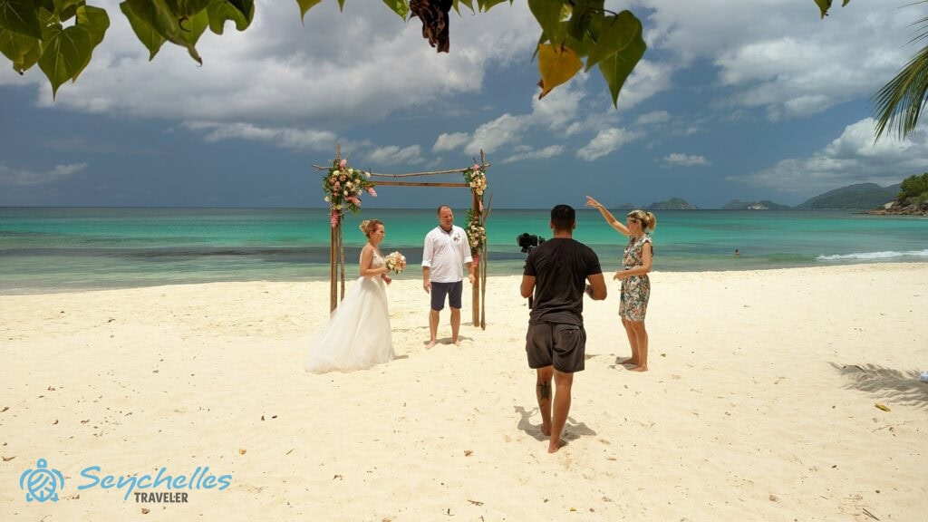 Réka az esküvői fotózáson a feldíszített boldogságkapu előtt álló párnak tolmácsolja a fotós kéréseit, Anse Louis parton.