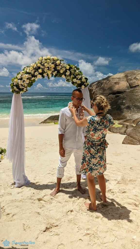 Réka az esküvői fotózáson megigazítja a férj nyakában lévő virágfüzért Baie Lazare tengerparton.