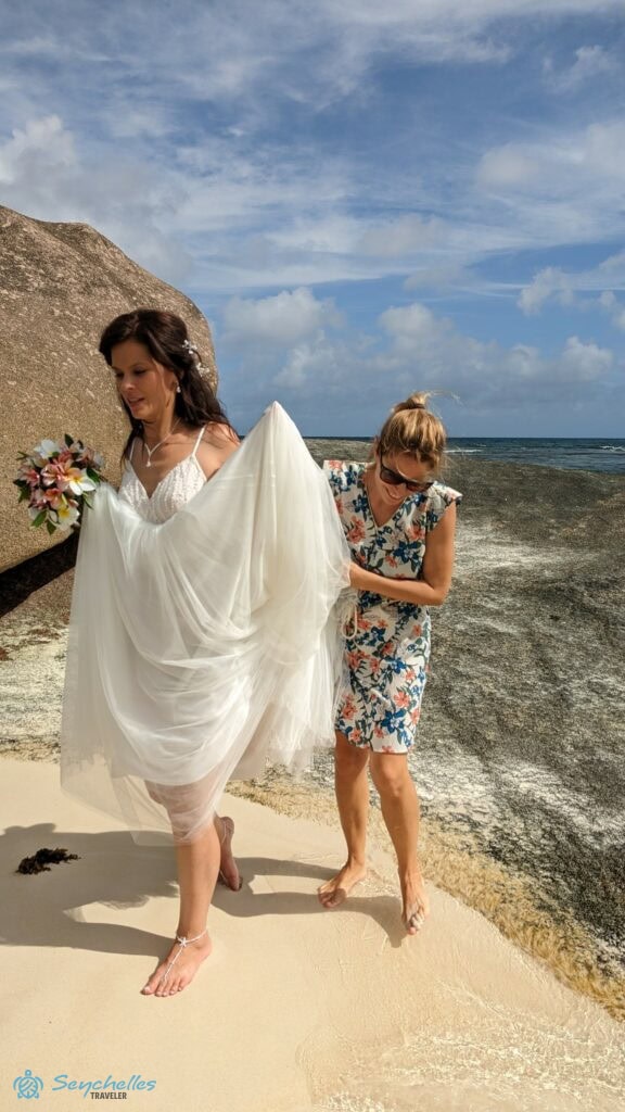 Réka a menyasszonynak segít a ruhájával az esküvői fotózáson Baie Lazare tengerparton.