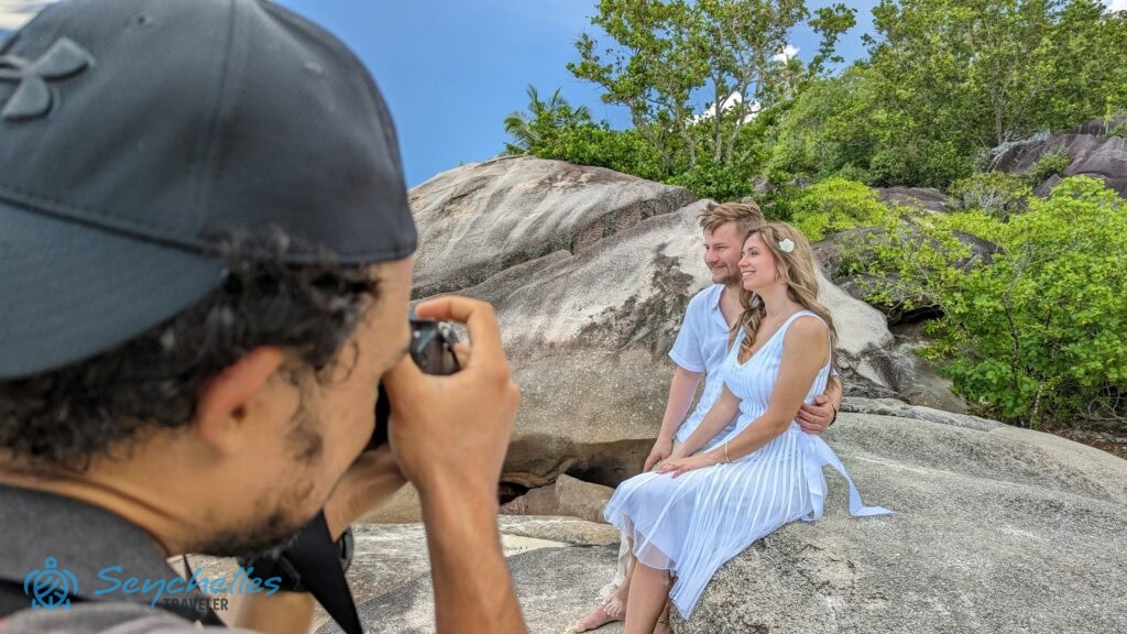 Közeli kép az esküvői fotósról, ahogy munka közben a házaspárt fényképezi Baie Lazare parton.